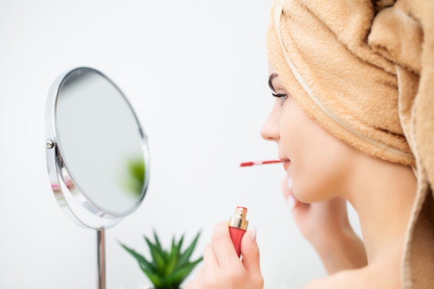 Vrij jonge vrouw zet make-up op het gezicht in de badkamer