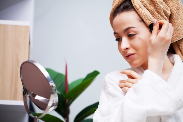 Vrij jonge vrouw zet make-up op het gezicht in de badkamer