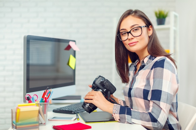 Vrij jonge vrouwenfotograaf met camera in bureau