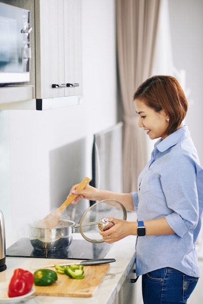 Vrij lachende jonge Vietnamese vrouw soep koken en soep mengen in pan