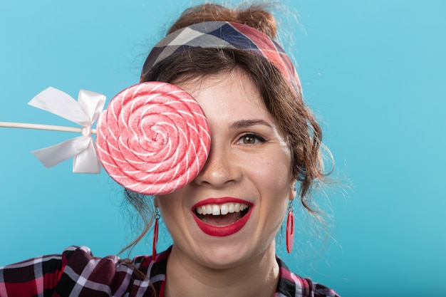 Vrij lachende jonge vrouw in een geruite overhemd sluit haar oog met grote kleurrijke lollies en poseren