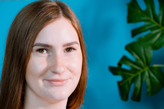 Vrij lachende vreugdevolle vrouw met bruin haar, tevreden kijkend naar de camera, gelukkig. Studio shot van knappe mooie vrouw op achtergrond studio muur en tropische bladeren.