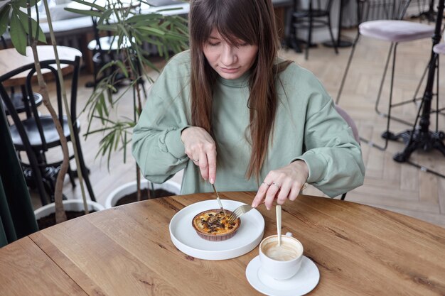 Vrij leuke vrouw zitten in lege café eet cake en drinkt koffie