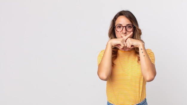 Vrij magere vrouw die er serieus uitziet en ontevreden is met beide vingers vooraan gekruist in afwijzing, en vraagt om stilte