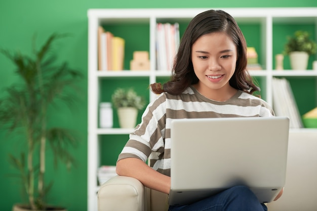 Vrij positieve jonge vrouw die thuis op laptop programmeert of huiswerk maakt