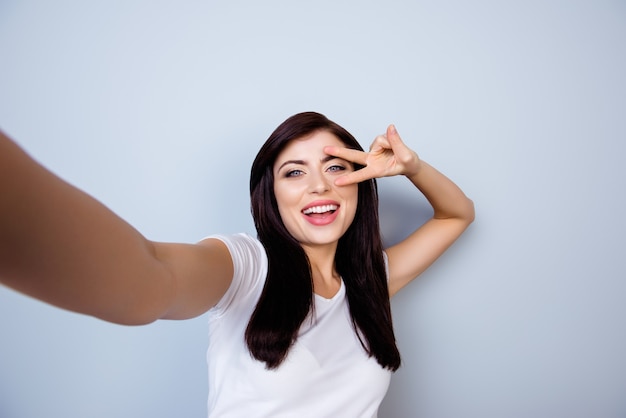 Vrij positieve vrolijke jonge vrouw die selfie met twee vingers maakt