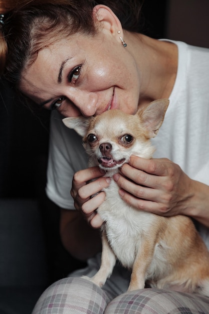 Vrij rijpe vrouw met Chihuahua-hond op donkere bank in huiswoonkamer. Vrouw van middelbare leeftijd en haar hondje Chihuahua. Concept huisdierenliefde en familievriend