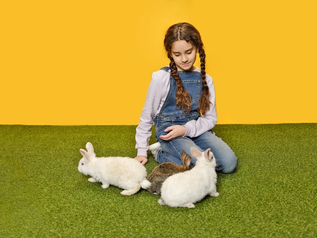 Vrij schattig klein meisje ligt te spelen met de konijntjes in de studio gele achtergrond