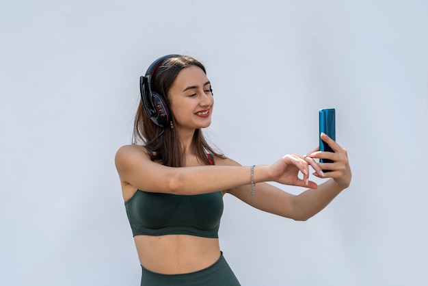 Vrij slanke vrouw in groene sportkleding en koptelefoon met telefoon luistert naar muziek na de training