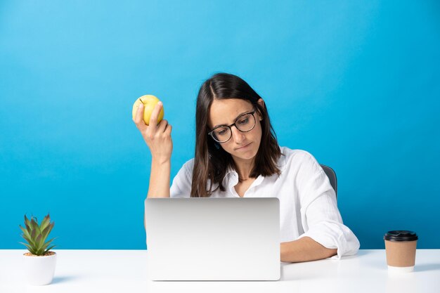 Vrij Spaanse vrouw die aan laptop werkt en appel vasthoudt