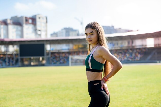 Vrij sportief meisje in het stadiongras gymnastiekoefeningen doen.