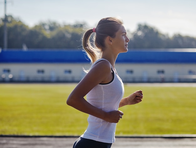 Vrij sportieve vrouw joggen in het park in het licht van de zonsopgang