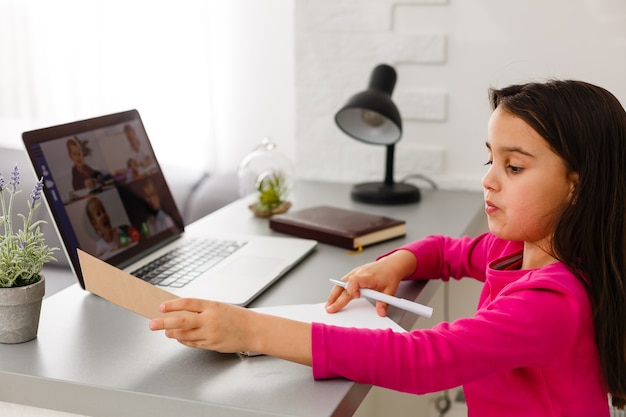 Vrij stijlvol schoolmeisje dat huiswerk wiskunde bestudeert tijdens haar online les thuis, sociale afstand tijdens quarantaine, zelfisolatie, online onderwijsconcept, thuisschooler