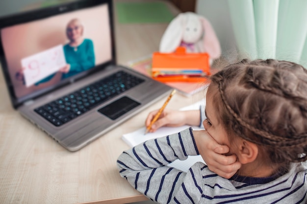 Vrij stijlvol schoolmeisje dat wiskunde bestudeert tijdens haar online les thuis, zelfisolatie