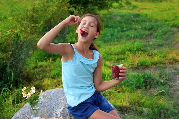 Foto vrij vrolijk kindmeisje dat rode aalbessen in tuin eet