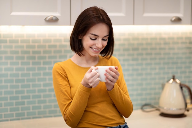 Vrij vrolijke jonge dame die thuis geniet van verse koffie in de ochtend