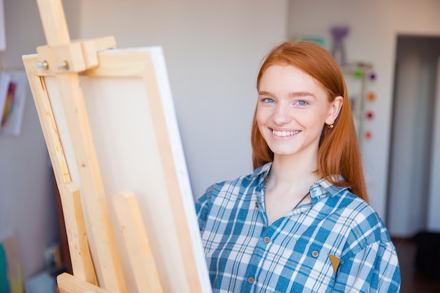 Vrij vrolijke jonge vrouwenschilder in het schilderen van geruit overhemd in kunststudio art