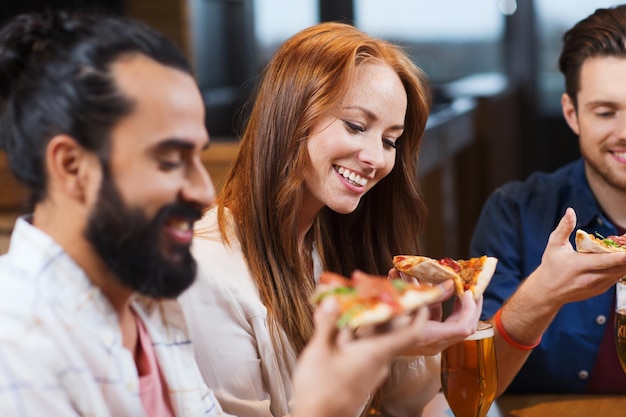 vrije tijd, eten en drinken, mensen en vakantie concept - lachende vrienden pizza eten en bier drinken in restaurant of pub