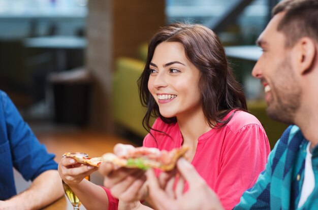 vrije tijd, eten en drinken, mensen en vakantie concept - lachende vrienden pizza eten en bier drinken in restaurant of pub