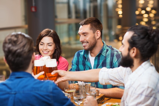 Vrije tijd, eten, eten en drinken, mensen en vakantieconcept - glimlachende vrienden die diner hebben en bier drinken bij restaurant of bar