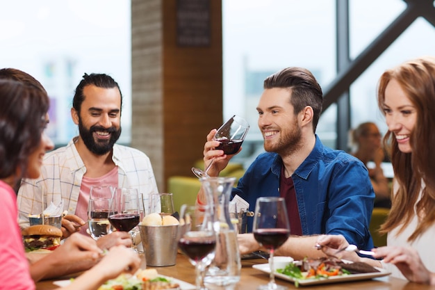vrije tijd, eten, eten en drinken, mensen en vakantieconcept - lachende vrienden die eten en rode wijn drinken in het restaurant