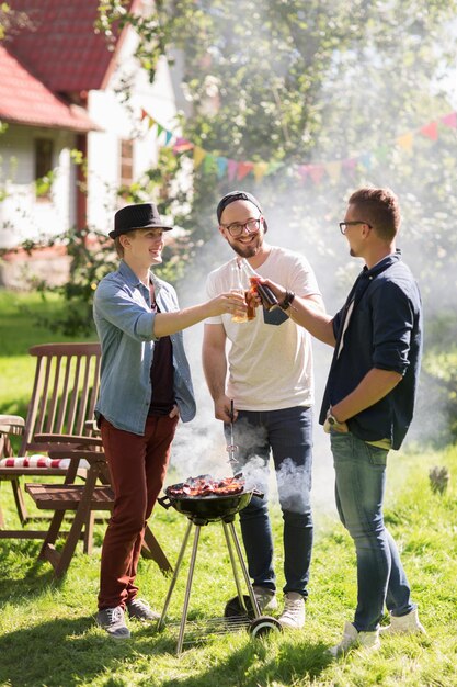 vrije tijd, eten, mensen, vriendschap en vakantie concept - gelukkige vrienden koken vlees op de barbecue en drinken bier op zomerfeest buiten