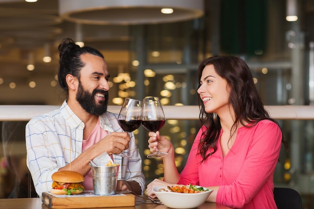 vrije tijd, feest, eten en drinken, mensen en vakantieconcept - lachend stel dat dineert en rode wijn drinkt op date in restaurant