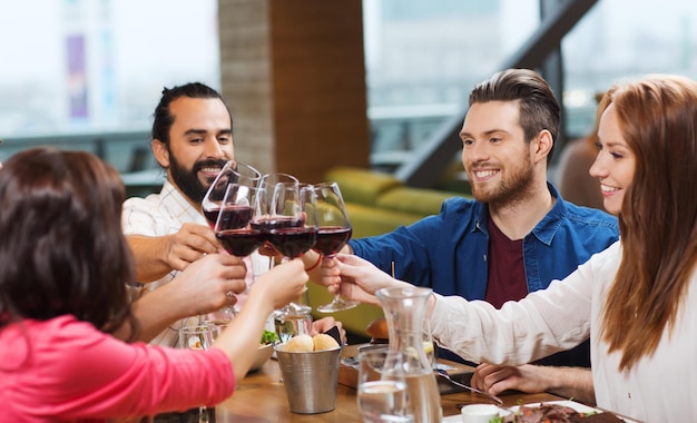 vrije tijd, feest, eten en drinken, mensen en vakantieconcept - lachende vrienden die eten en rode wijn drinken in het restaurant