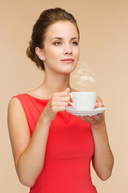 vrije tijd, geluk en drank concept - lachende vrouw in rode jurk met kopje koffie