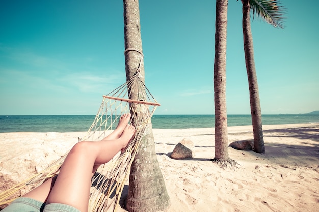 Vrije tijd in de zomer - Mooie Gelooide benen van sexy vrouwen. ontspan op hangmat bij zandig tropisch strand. vintage kleurstijlen