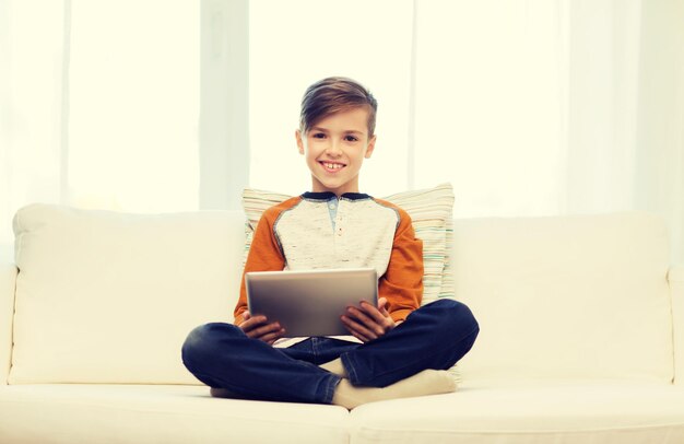vrije tijd, kinderen, technologie en mensenconcept - glimlachende jongen met de computer van tabletpc thuis