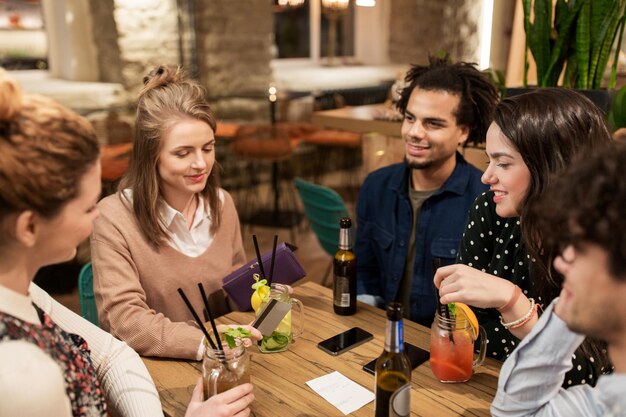 vrije tijd, mensen en vakantieconcept - gelukkige vrienden met drankjes, creditcard en rekening in bar of café