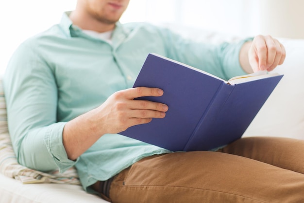 vrije tijd, onderwijs, literatuur en thuisconcept - close-up van de mens en zittend of liggend op de bank en thuis een boek lezend