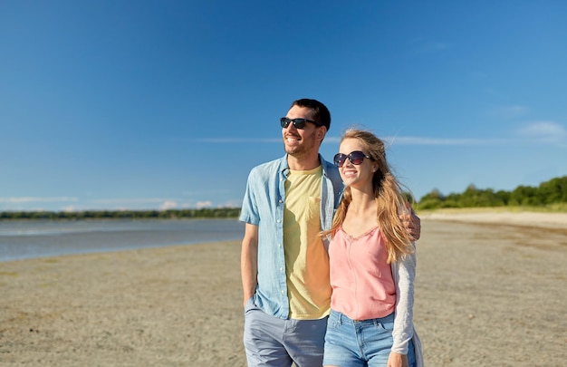 vrije tijd, relatie en mensen concept - gelukkig paar in zonnebril knuffelen op het zomerstrand