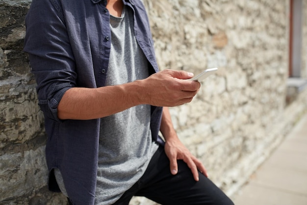 vrije tijd, technologie, communicatie en mensenconcept - close-up van de mens met smartphone bij stenen muur op straat