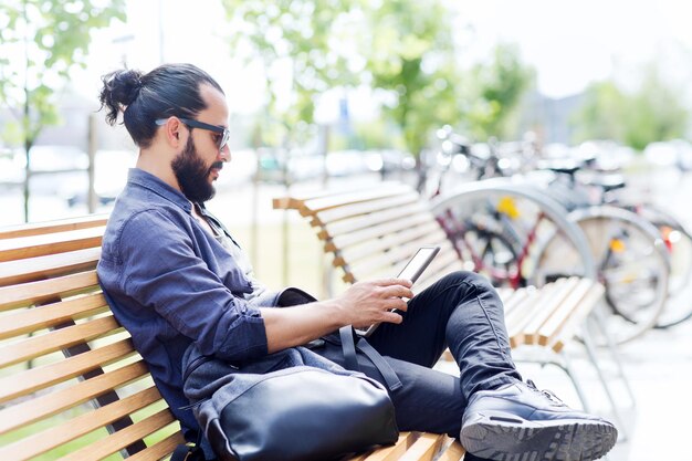 vrije tijd, technologie, communicatie, reizen en mensenconcept - man met tablet pc-computer en tas zittend op straatbankje in de stad