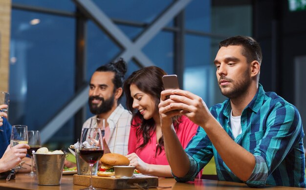 vrije tijd, technologie, internetverslaving, levensstijl en mensenconcept - man met smartphone en vrienden in restaurant