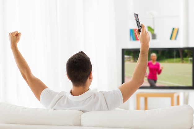 vrije tijd, technologie, massamedia en mensenconcept - man met afstandsbediening die naar sportkanaal op tv kijkt en thuis van achteren ondersteunt