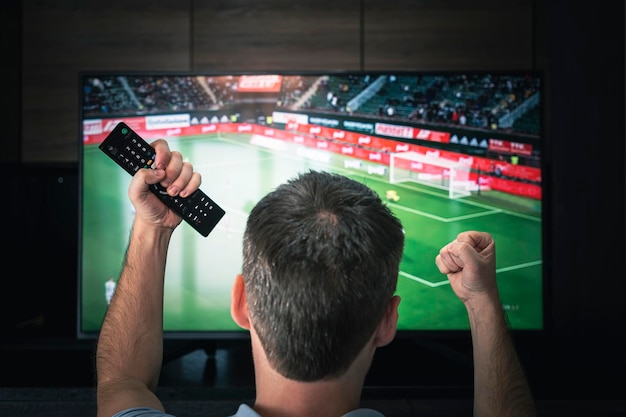 Vrije tijd technologie sport entertainment en mensen concept man met afstandsbediening kijken naar voetbal of voetbalwedstrijd op tv thuis Opgewonden voetbalfan kijken naar een wedstrijd op televisie