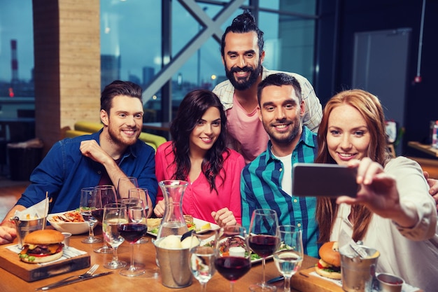 Foto vrije tijd, technologie, vriendschap, mensen en vakantieconcept - gelukkige vrienden die dineren en selfie nemen via smartphone in restaurant