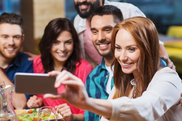 vrije tijd, technologie, vriendschap, mensen en vakantieconcept - gelukkige vrienden die eten en selfie maken met de smartphone in het restaurant
