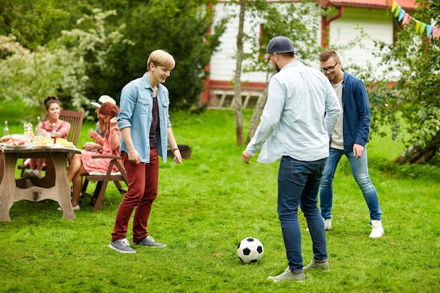 vrije tijd, vakantie, mensen en sportconcept - gelukkige vrienden voetballen op zomertuinfeest