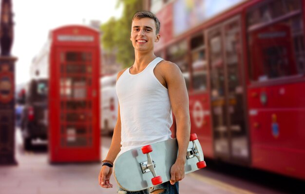 vrije tijd, zomervakantie, sport, reizen en mensen concept - lachende man of tiener met skateboard met skateboard op london city street