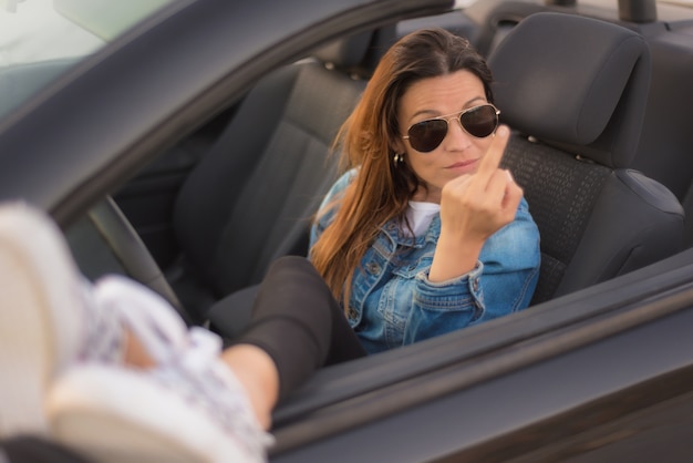 Vrije vrouw die middelvinger toont die van haar convertibele auto geniet. Vrijheid vrouw concept.