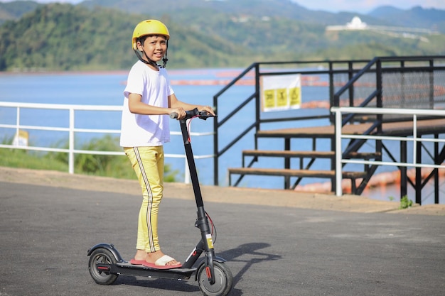 Vrijetijdsconcept voor jongeren. Volledig portret van een opgewonden jongen die een zwarte e-scooter berijdt in het rivierpark.