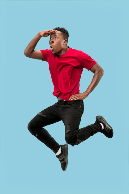 Vrijheid in beweging en voorwaartse beweging. De blij verraste jonge afrikaanse man die tegen een blauwe studioachtergrond springt Runnin man in beweging of beweging. Menselijke emoties en gezichtsuitdrukkingen