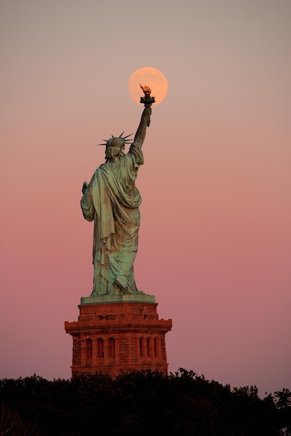 Vrijheidsbeeld en volle maan bij zonsondergang in New York City