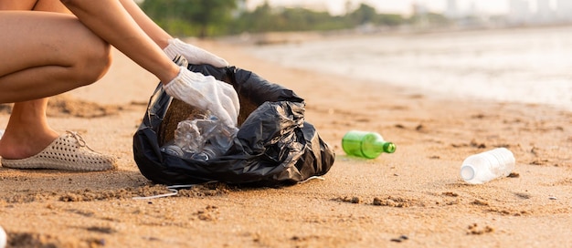 Vrijwillige vrouw plukt plastic fles in zwarte vuilniszak om het strand schoon te maken