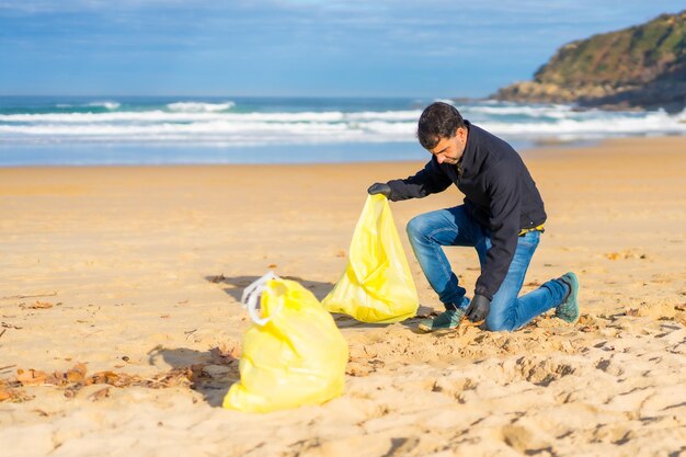 Vrijwilliger die plastic verzamelt uit het zand op het strand Ecologieconcept zeeverontreiniging