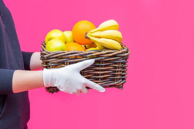 Vrijwilliger in handschoenen houdt mand met kruidenierswaren met fruit